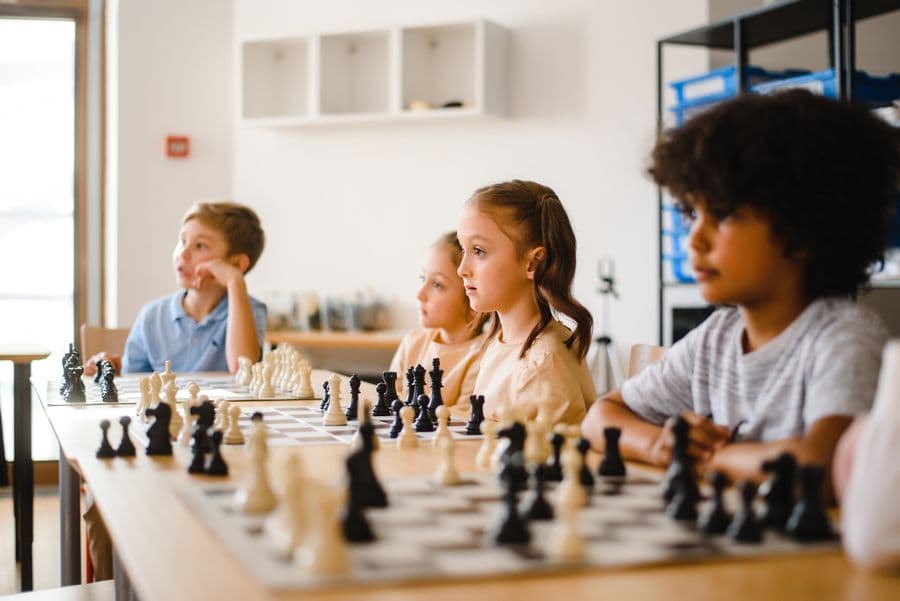 Children concentrating at a row of chess boards in a bright classroom.